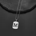 Detailed view of a silver-toned stainless steel dog tag necklace featuring a cut-out letter M - Letter M