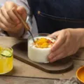 Lifestyle view of a clear glass dessert bowl filled with creamy yogurt and mango chunks - Transparent