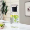 Detailansicht der skandinavischen Glas-Wasserkaraffe mit schwarzem Deckel und Zitrone. - Zylindrischer Stil Mit Hülle / 1000ml