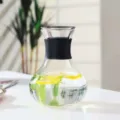 Detailed view of clear glass cold water pitcher with black silicone grip and lemon slices inside. - Round-Bellied Style With Sleeve / 1000ML