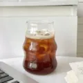 Einzigartiger wellenförmiger Glas-Wolkenbecher mit Eiskaffee auf weißem Schreibtisch - 500ml / Glatte Oberfläche Einzelbecher