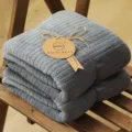 Soft grey coral fleece bath towel with vertical stripes and brand tag on a bench - 80*150cm / Gray