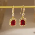 Close-up of elegant gold drop earrings with emerald-cut red zircon and crystal halo - Hook Earrings Style (80492) / Red