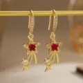 Detailed macro of gold star earrings featuring vibrant red zircon and shooting stars. - Hook Earrings Style (80495) / Red