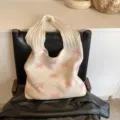 Crèmekleurige gebreide draagtas met roze strikpatroon op een zwarte leren stoel geplaatst - Beige met roze strik