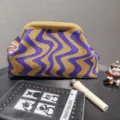 Detail view of a knitted wavy pattern clutch bag with cosmetic accessories on a desk - Purple & Yellow