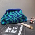 Detailed macro view of blue and green wavy striped knitted cosmetic bag on grey surface - Blue