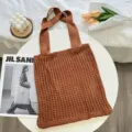 Braune gestrickte Netztasche in einer gemütlichen Szene mit floralen Requisiten - Karamellbraun