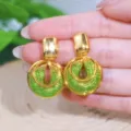 Vista detallada de pendientes dorados con malla verde brillante sostenidos a mano. - Gold Green Rhinestone Style (E4113) / Dorado