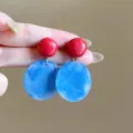 Close-up of elegant red and blue marbled acetate earrings held by hand. - Half-sphere and Large Disc Pendant Style (E5030) / Red Blue