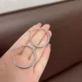 Detail showing a pair of large silver polished minimalist hoop earrings held in a hand. - Classic Closed Hoop Style (E0517) / 3cm / Silver