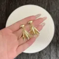Gros plan de boucles d'oreilles feuilles dorées tenues à la main pour l'échelle et détail - Boucles d'Oreilles à Gland en Feuilles Multi-Couches Robustes (E5008) / Or