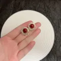 Elegant Ankara red crystal earrings with gold finish, showcased on a hand model - Round Pavé Ear Clip (E4144) / Dark Red