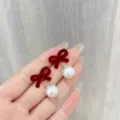 Elegant red velvet bow-knot earrings with round white pearl drops displayed on a hand - Flocked Bow Artificial Pearl Style (E4170) / Red