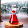 Detailed shot of a red and clear crystal angel figurine on a rustic wooden base. - Red Angel Ornament