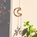 Detailed view of a moon-shaped crystal suncatcher with rainbow reflections in sunlight - Moon