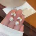 Primo piano di orecchini a lobo con foglie luccicanti e pendenti di perle bianche - Stile Perla Foglia Strass (E4902) / Oro