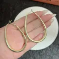 Macro view of large gold-tone oval hoop earrings held in hand for scale detail shot. - 4.4cm/6.4cm / Gold