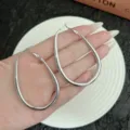 Close-up of large minimalist silver geometric oval hoop earrings held over a white plate - 4.4cm/6.4cm / Silver