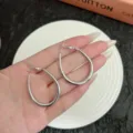Detailed macro view of stylish silver geometric teardrop hoop earrings held in hand - Small (4.8cm/3.3cm) / Silver