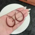 Close-up detail of stylish Ancora Red oval oil-drop hoop earrings held by hand for scale - Small (4.8cm/3.3cm) / Ancorra Red