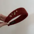 Gros plan d'un serre-tête large en peluche rouge avec d'élégants charms dorés. - Design Cheval Chanceux / Rouge