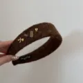 Gros plan d'un serre-tête marron en peluche avec breloques dorées et logo - Design Cheval Chanceux / Marron