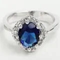 Elegante anillo de latón plateado con cristal azul ovalado y halo de circonitas claras - Talla 9 / Azul