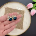 Dettaglio ravvicinato di orecchini a fiore dorati con cristalli quadrati blu intenso - Oro Blu (E2092)
