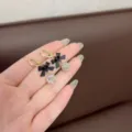 Nahaufnahme von funkelnden Zirkonia-Ohrringen mit schwarzen Schleifen in der Hand. - Schleife Huggie Ohrring (2116) / Gold/Schwarz