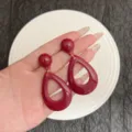 Elegant burgundy teardrop dangle earrings showcased on a hand against white plate - Burgundy