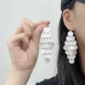 Close-up view of white tiered shell disk tassel earrings with elegant gold studs. - Stud Earrings / White