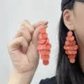 Detail view of vibrant coral disc tassel earrings worn by a model for a stylish vacation look - Stud Earrings / Orange