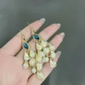 Primo piano dettagliato di eleganti orecchini a pavone dorati con perle e cristalli blu - Stile Pendente Perla Forma Pavone (E1668) / Oro