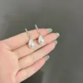 Vista dettagliata di orecchini a goccia con perle e cristalli scintillanti in mano. - Stile Perla a Goccia Barocca (E1792) / Argento