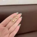 Dettaglio di orecchini stile francese con strass e perle centrali sulla mano - Stile Perla Croce Incrociata (E1809) / Oro champagne