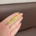 Close-up of vibrant neon green enamel geometric hoop earrings held in hand for detail - Light Green