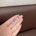 Close-up of purple enamel hoop earrings held on fingers for size reference. - Purple