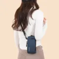 Compact blue vertical crossbody phone bag for sports and daily travel on model - One Size / Dark Blue