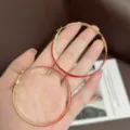 Large fashion red enamel and gold hoop earrings held in hand for size comparison. - Enamel Hoop Style (E3782) / 5.7cm / Red Gold