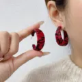 Close-up of Ancora red C-shaped earrings with black animal print texture on a model. - C-Shape Earrings Style (E4424) / One Size / Red Black Texture