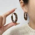 Close-up of leopard print furry hoop earrings worn on ear and held by hand. - Hoop Style (E4421) / 4cm / Brown Leopard