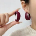 Detailed view of textured burgundy Ankara red C-shaped earrings being worn and held - C-Shape Earrings Style (E4424) / One Size / Solid Burgundy