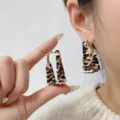 Close-up of geometric square leopard print earrings on model's ear and held in hand - Geometric Trapezoid Style (E4418) / Light Coffee Leopard