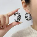 Detailed close-up of textured zebra-patterned C-shaped hoop earrings worn on the ear. - C-Shape Earrings Style (E4424) / One Size / White and Black Zebra Print
