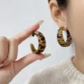 Close-up detail shot of stylish C-shaped hoop earrings with leopard print texture on a model - C-Shape Earrings Style (E4424) / One Size / Yellow and Black Leopard