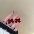 Orecchini a lobo con fiocco di velluto rosso tenuti in mano su sfondo neutro - Stile Fiocco Floccato Rosso (E1600) / Rosso