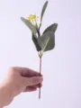 Hand holding a short artificial eucalyptus stem with realistic green leaves and yellow berries. - With Berries