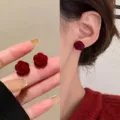 Elegant dark red velvet rose-shaped stud earrings shown on hand and worn on model's ear - Red Rose Style (E3572) / Red