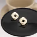 Elegant cream white knotted flower stud earrings with gold trim on glossy black stand - Twisted Floral Stud Earrings (E3702) / White